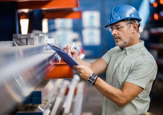 Homme portant un casque bleu et tenant une tablette, inspectant des matériaux dans un entrepôt avec un WMS